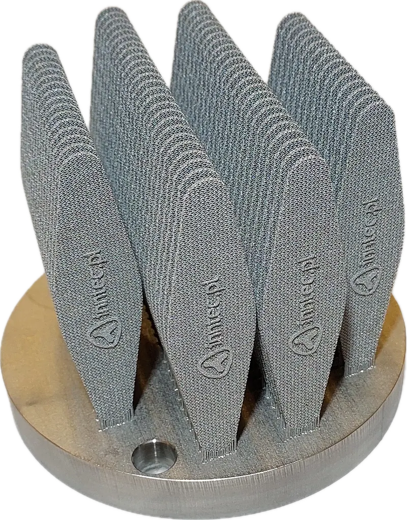 Metalowe wydruki 3D z logo inntec.pl na płycie roboczej, wykonane w technologii LPBF